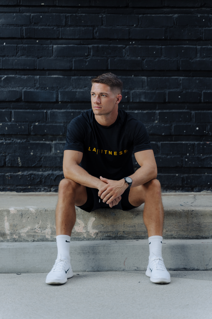 Men’s black S/S Raglan Perforated Knit Tee with yellow text "LA | FITNESS"